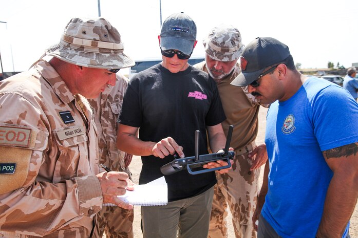 Men watch drone on screen.