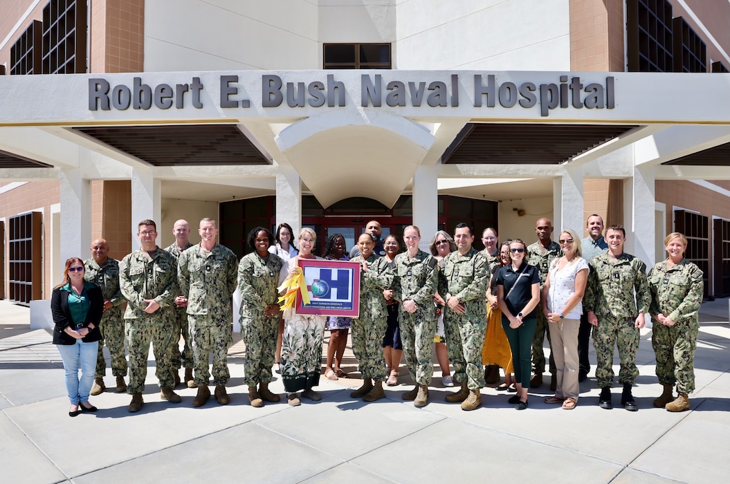 Staff and leadership from Naval Hospital Twentynine Palms gather in front of the hospital on August 20 with Commanding Officer Capt. Janiese Cleckley, Executive Officer Capt. Candace Foura, Command Master Chief HMCM Richard Moreno, Director for Public Health Cmdr. Christina Carter, and Public Health Specialist Tanya Stuckey to celebrate earning the Blue-H Award at the Gold Star level for the 14th consecutive year.