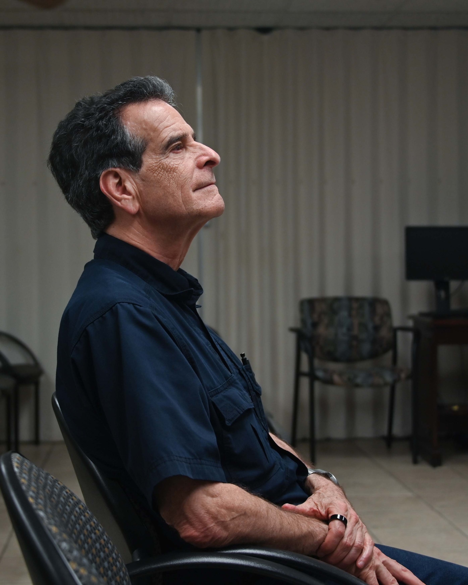 Man sits in a chair watching a briefing