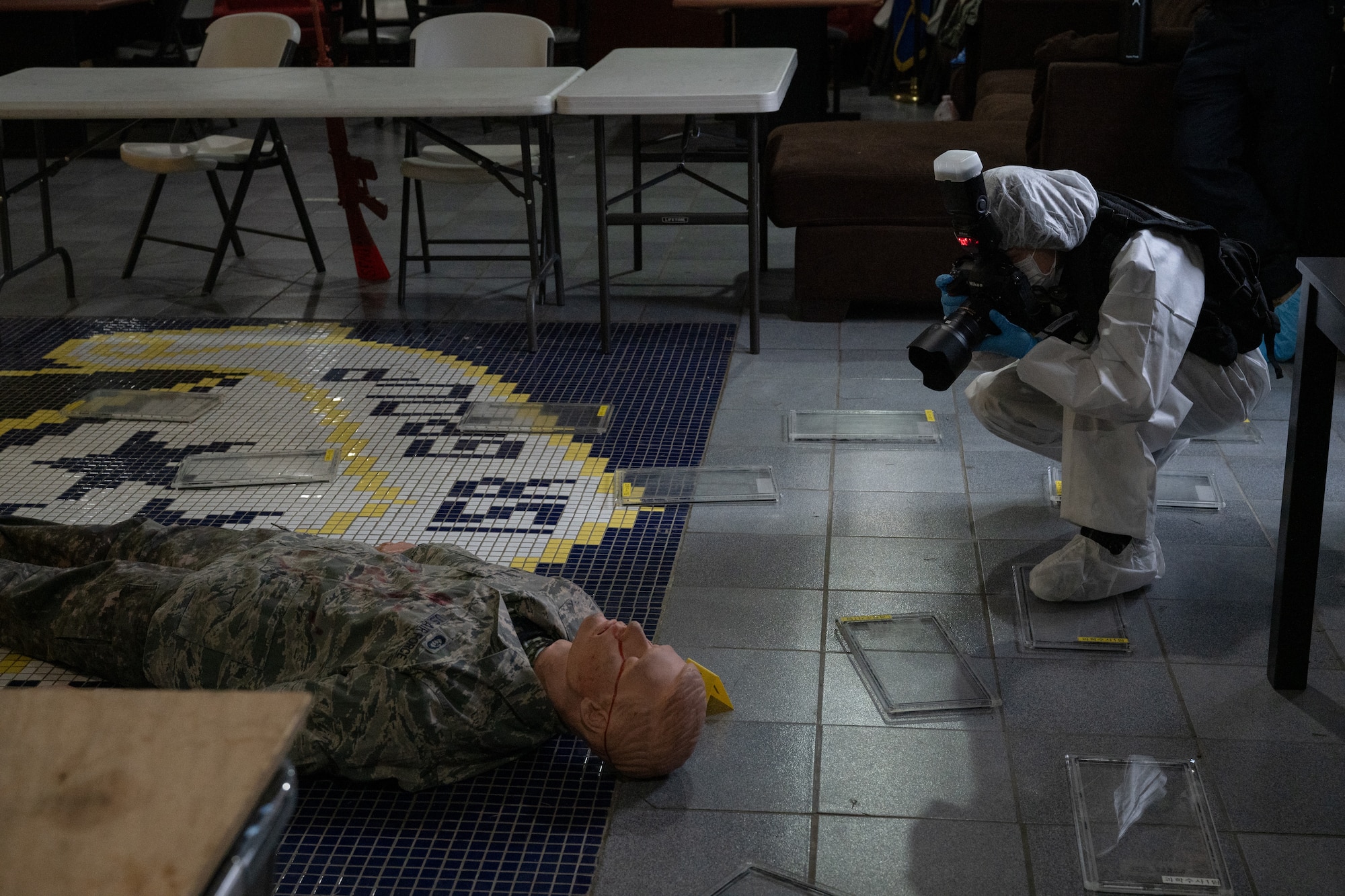 A crime scene investigator photographs a mannequin during a training scenario.