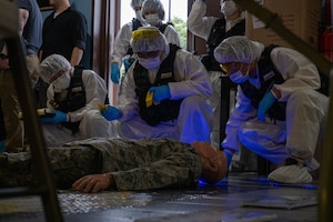 Crime scene investigators search for evidence around a mannequin during a training scenario.