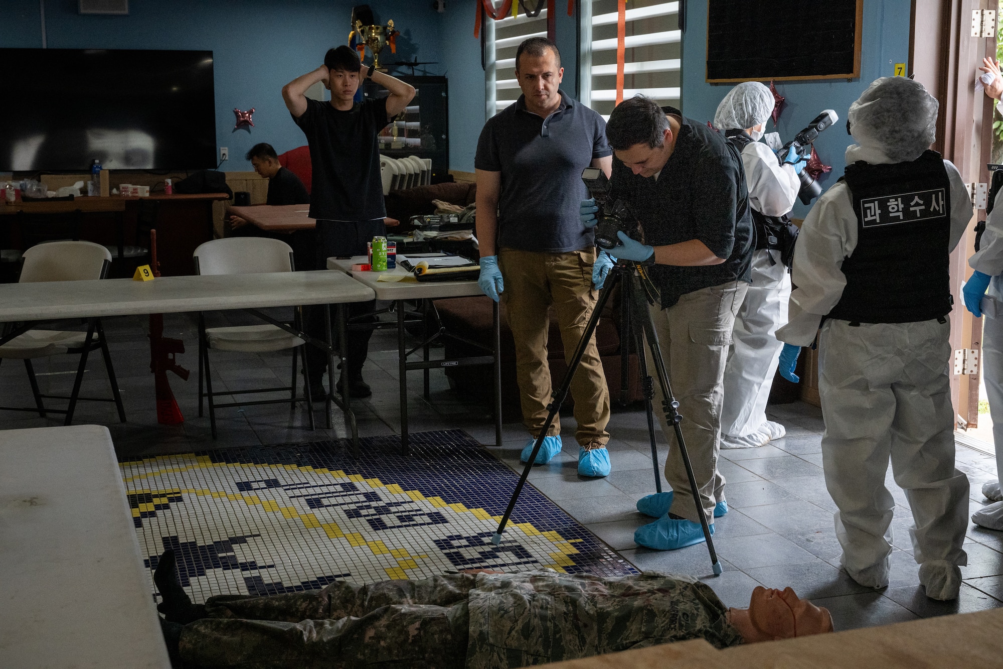 A crime scene investigator takes photos of a mannequin during a training scenario.
