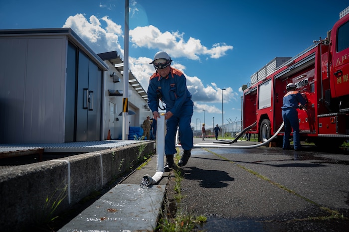 A Hachinohe City Fire Department firefighter rolls and drains a water line during a fuel tank fire drill at Hachinohe City, Japan, Sept. 3, 2025.