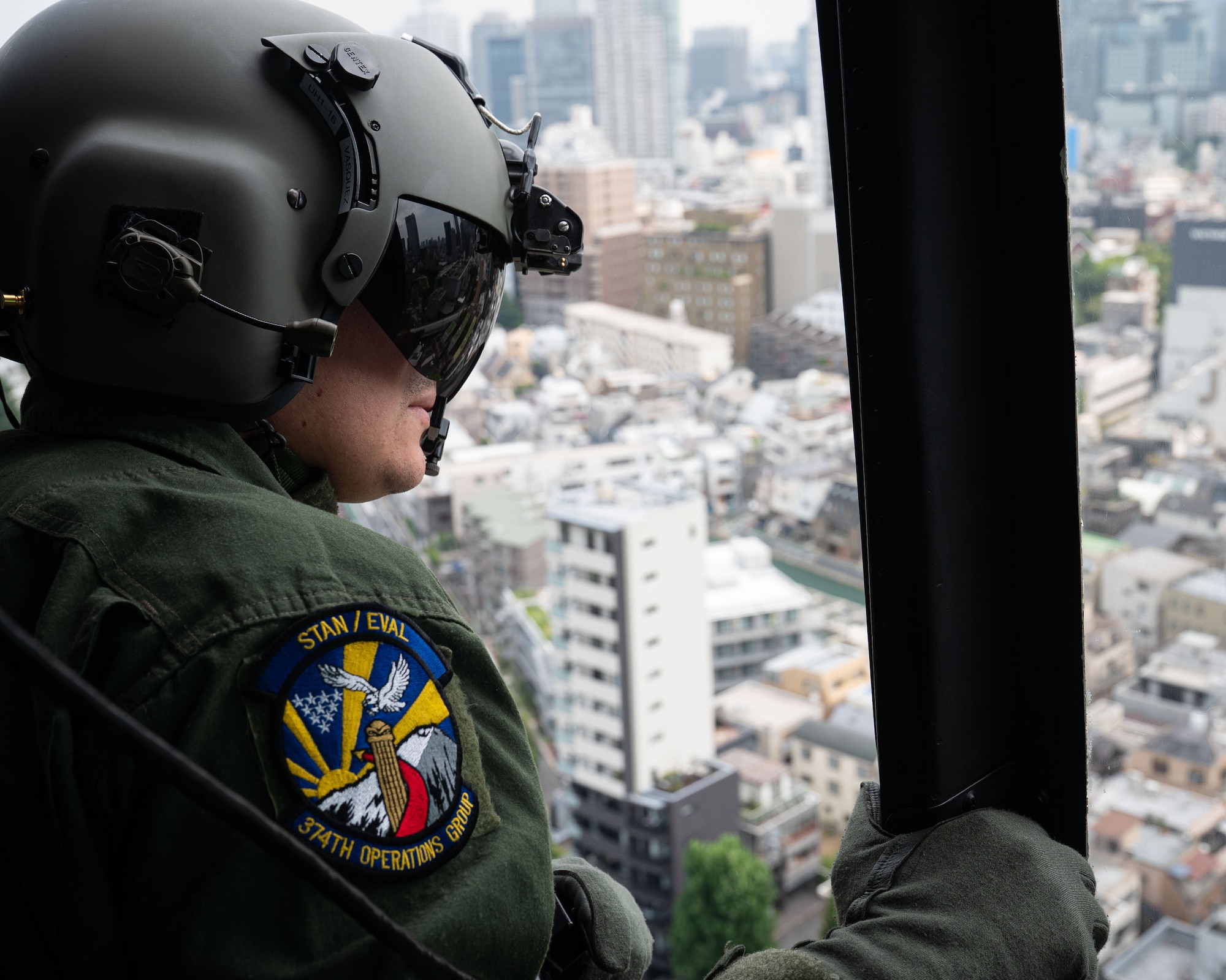 A servicemember looks out of a helicopter at the cityscape
