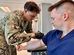 GUANTANAMO BAY, Cuba (August 28, 2025) – Hospital Corpsman 2nd Class Clayton VanStry demonstrates the process to collect fresh whole blood from Hospital Corpsman 3rd Class Joshua Moulton at U.S. Naval Hospital Guantanamo Bay, August 28, 2025. Whole blood transfusion capability provides a critical life-saving option in combat and austere environments, directly supporting operational readiness. (U.S. Navy photo by Emily McCamy)