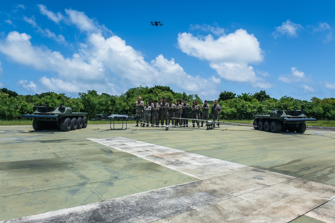 U.S. Marines with 4th Marine Regiment, 3d Marine Division pose for a photo with various unmanned systems on Camp Schwab, Okinawa, Japan, Aug. 13, 2025. This class, which certifies Marines to fly multiple variants of sUAS, was the first time untethered drones were flown over a military installation on Okinawa under the Secretary of Defense's new guidance, which seeks to expand the use of small, American-made drones to enhance military capabilities. From left to right, the unmanned platforms are the Mission Master Silent Partner Unmanned Ground Vehicle, the Tactical Resupply Unmanned Aircraft System (TRUAS), the RQ20-B Puma, the Stalker UAS, and the in-flight, Skydio X2D. (U.S. Marine Corps photo by Cpl. Joaquin Dela Torre)
