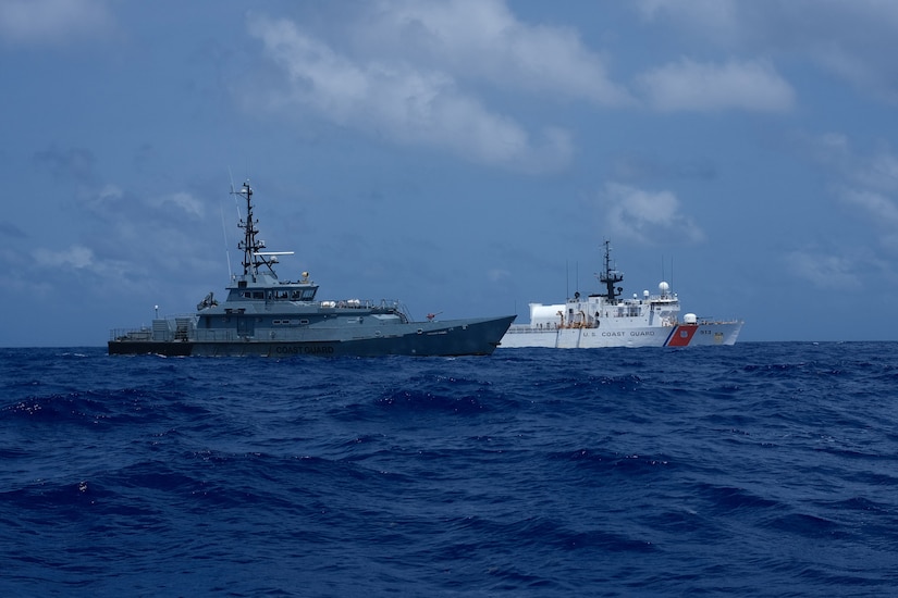 A Coast Guard helicopter hoovers over the deck of a large white Coast Guard ship.