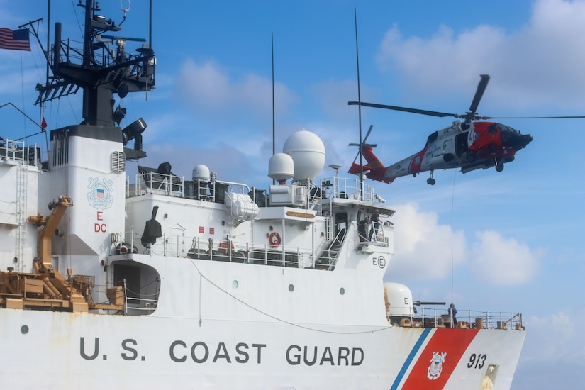 A large gray foreign military ship, left, sails in the ocean beside a white Coast Guard ship.