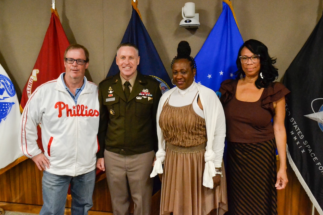 Four people pose for photo in front of military flags,