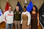 Four people pose for photo in front of military flags,