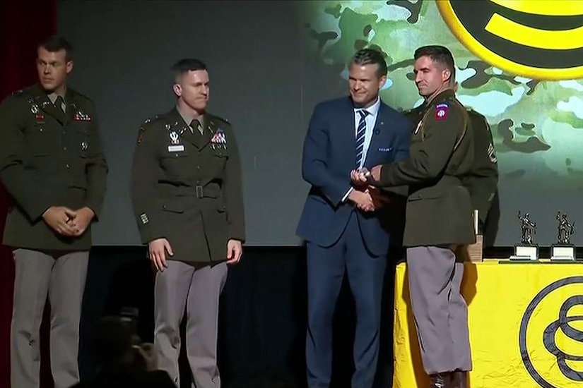 The defense secretary shakes hands with a graduate on stage.