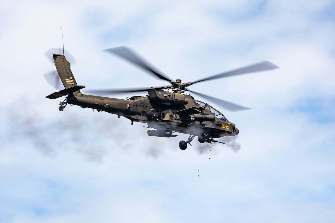 A helicopter in flight shoots, leaving smoke behind, against a partly cloudy sky during the day.