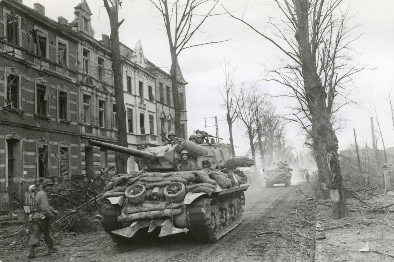 A tank rolls along a dirt road in a destroyed city.