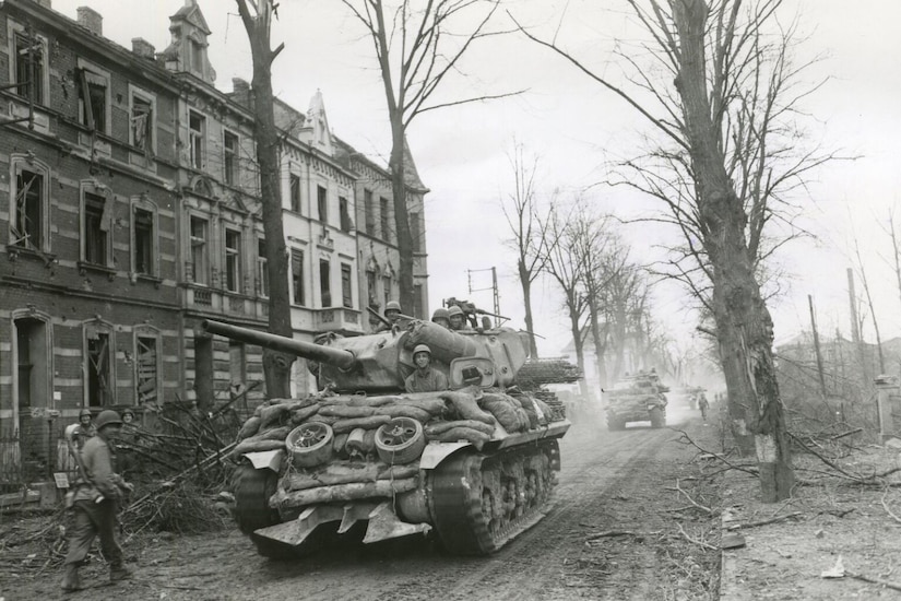 A tank rolls along a dirt road in a destroyed city.