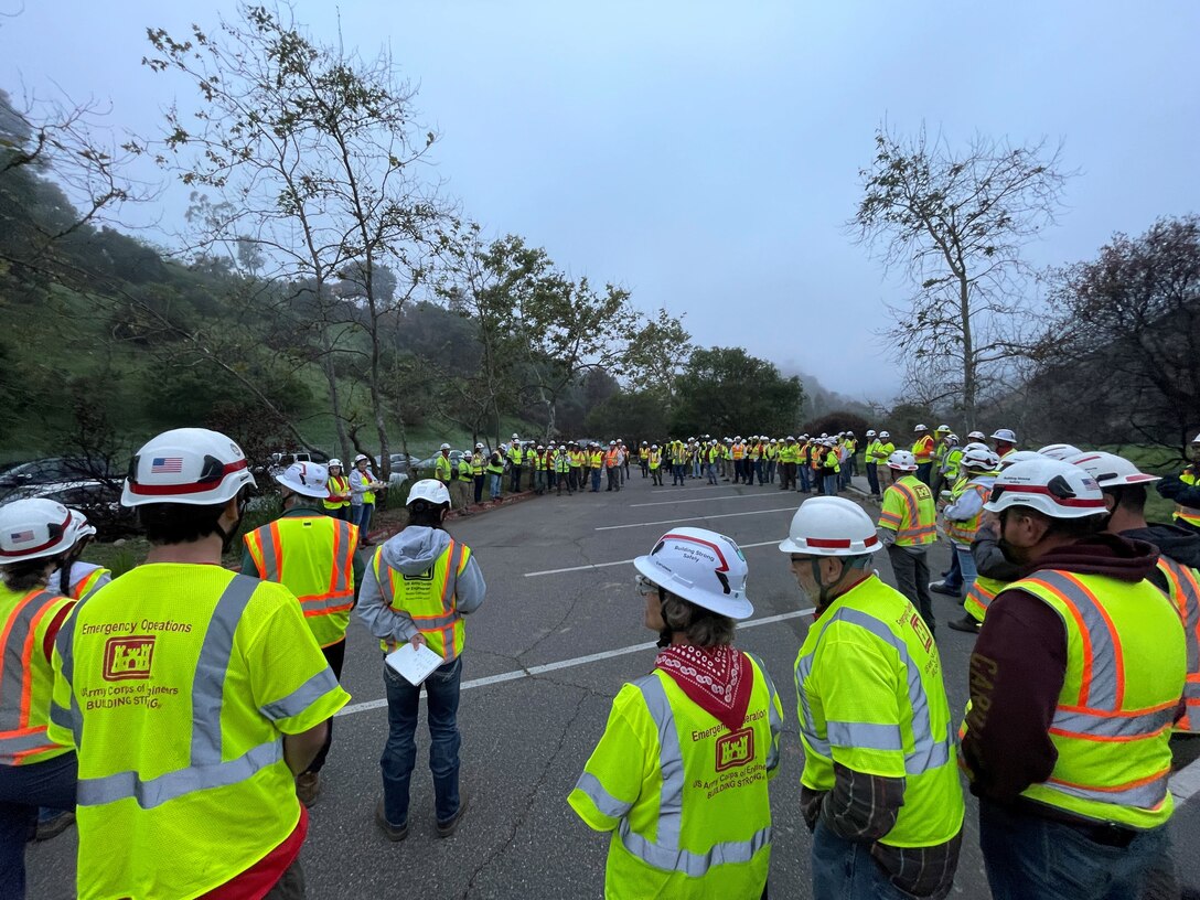 QAs meet for their morning meeting, April 12, 2025, in a parking lot in Pacific Palisades, Calif.  These QAs were working the Palisades debris removal mission, part of the USACE Southern California wildfires recovery mission after wildfires burned parts of Los Angeles in January 2025. Photo by Forrest Luna.