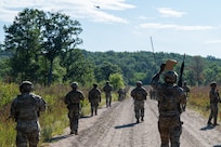Defender Airmen patrol along a dirt road within Camp Ripley Training Center.