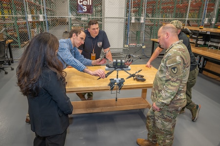 A group of people standing around a drone watching a demonstration.