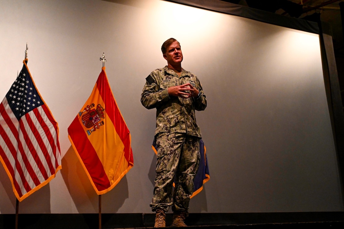 Rear Adm. Rosen stands on a stage explaining to a crowd.