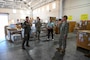 A Navy officer points at equipment in a warehouse to the Admiral.