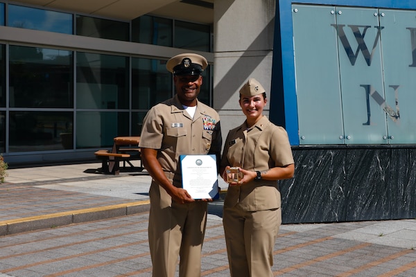 SILVER SPRING, Md. (Sept. 3, 2025) Master Chief Hospital Corpsman Phillip Jean-Gilles, command master chief (CMC) of Naval Medical Research Command (NMRC), poses with his certificate of reenlistment and Lt. Sara Tuck stands along side him with a gift he presented her, following his reenlistment ceremony. Immediately following his reenlistment, Jean-Gilles relinquished his position as CMC to Master Chief Hospital Corpsman Christopher Cariss during a change of office ceremony. NMRC, headquarters of Navy Medicine Research & Development, is engaged in a broad spectrum of activity from basic science in the laboratory to field studies in austere and remote areas of the world to investigations in operational environments. In support of Navy, Marine Corps and joint U.S. warfighter health, readiness and lethality, researchers study infectious diseases, biological warfare detection and defense, combat casualty care, environmental health concerns, aerospace and undersea medicine, operational mission support and epidemiology. (U.S. Navy photo by Aleece Williams/Released)