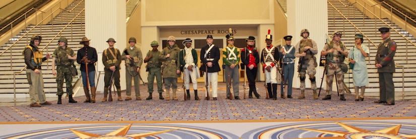 Marines pose for a photo in a convention center while wearing various historical uniforms.