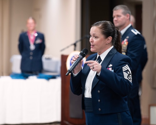 A woman in dress uniform and many stipes on her sleeve gestures as she speaks into a microphone.
