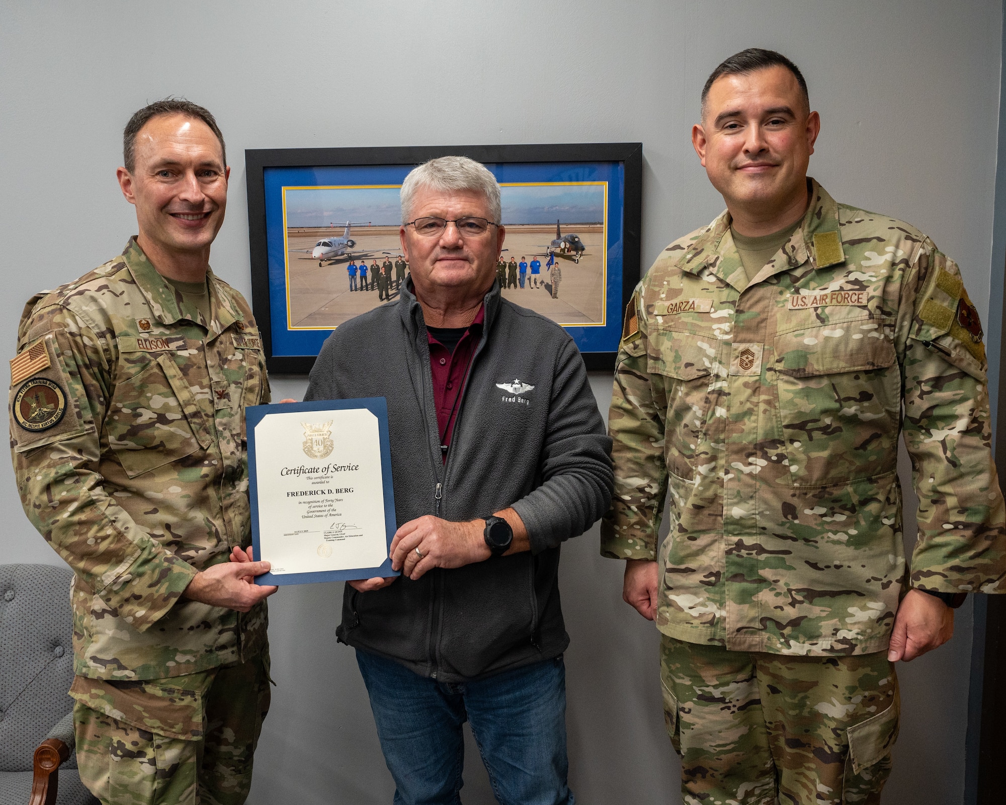 U.S. Air Force Col. Tyler Ellison, 47th Flying Training Wing (FTW) commander, left, and Chief Master Sgt. Erik Garza, 47 FTW command chief, right, present Frederick Berg, 47th Student Squadron civilian simulator instructor, center, with a certificate of service, at Laughlin Air Force Base, Texas, Aug. 26, 2025. The certificate of service celebrated 40 years of service to the U.S. government, 12 years were active-duty service with the Air Force. (U.S. Air Force photo by Staff Sgt. Nicholas Larsen)