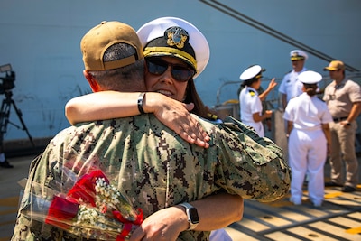 Uniformed service members hug and hold flowers standing in front of ship.