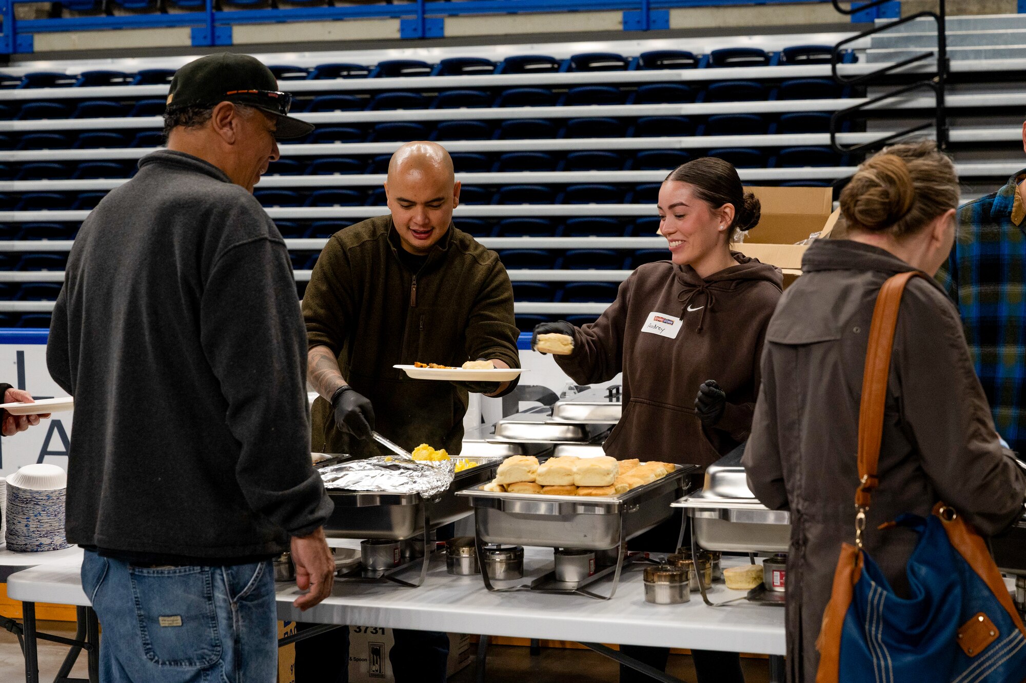 U.S. Air National Guard Tech. Sgt. Kenneth Santiago and Senior Airman Audrey Winterton of the 168th Logistics Readiness Squadron talk with Veterans while serving breakfast during the 2025 Veterans Stand Down at the Carlson Center in Fairbanks, Alaska.