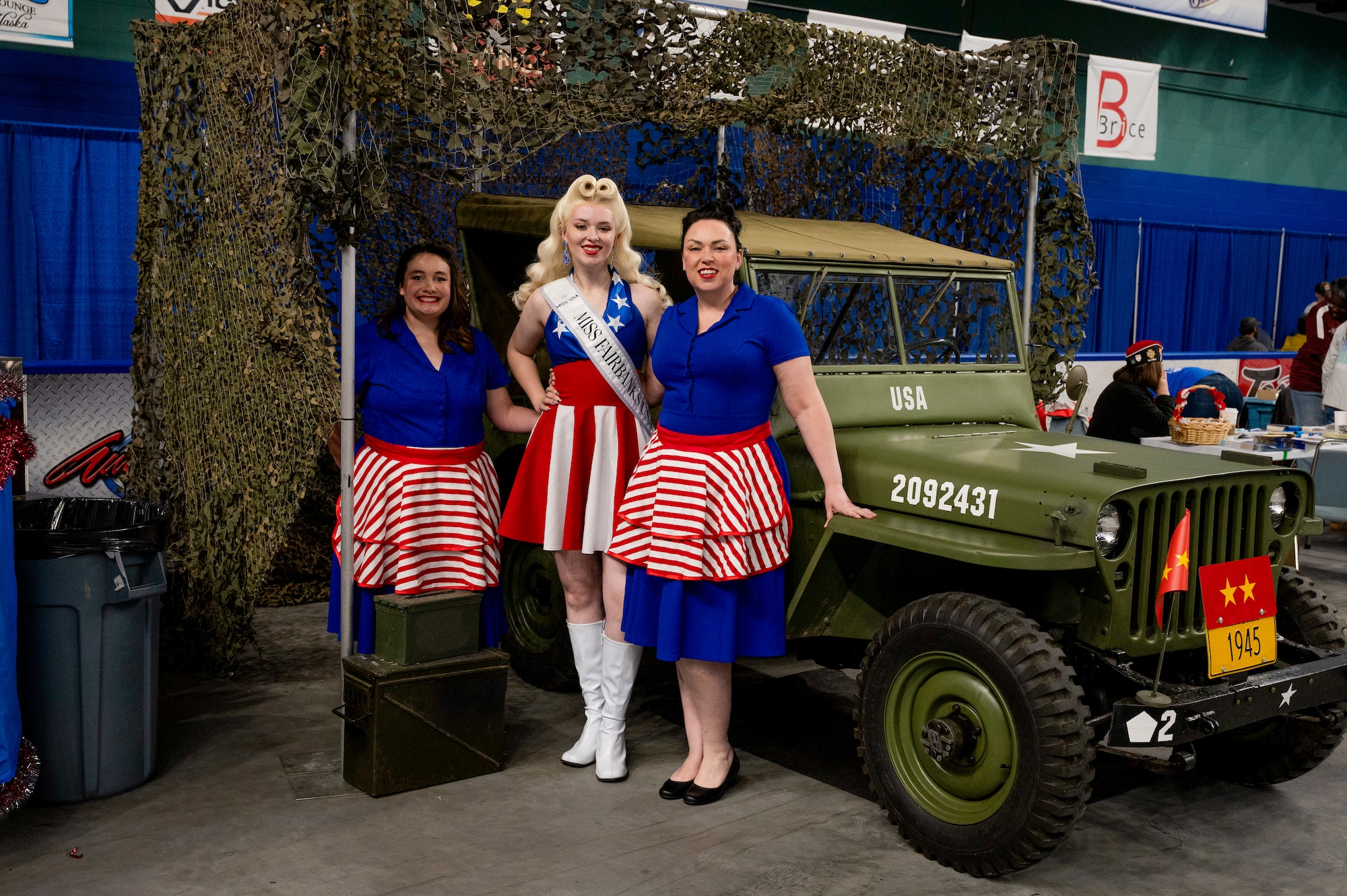 Maylaynee White, Miss Fairbanks, and a civilian maintenance worker at the 168th Civil Engineering Squadron, center, stands with her mother and a friend in front of a 1945 Jeep during the 2025 Fairbanks Veterans Stand Down at the Carlson Center in Fairbanks, Alaska.