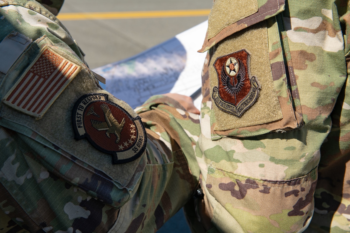 Two uniformed men with decorated patches on their sleeves point at a map.