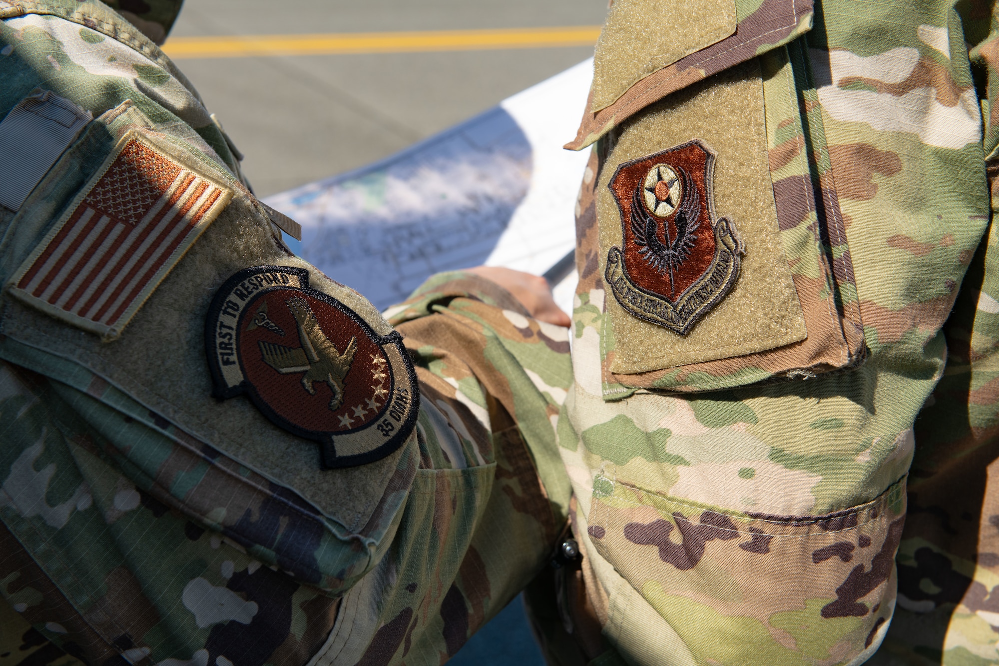 Two uniformed men with decorated patches on their sleeves point at a map.