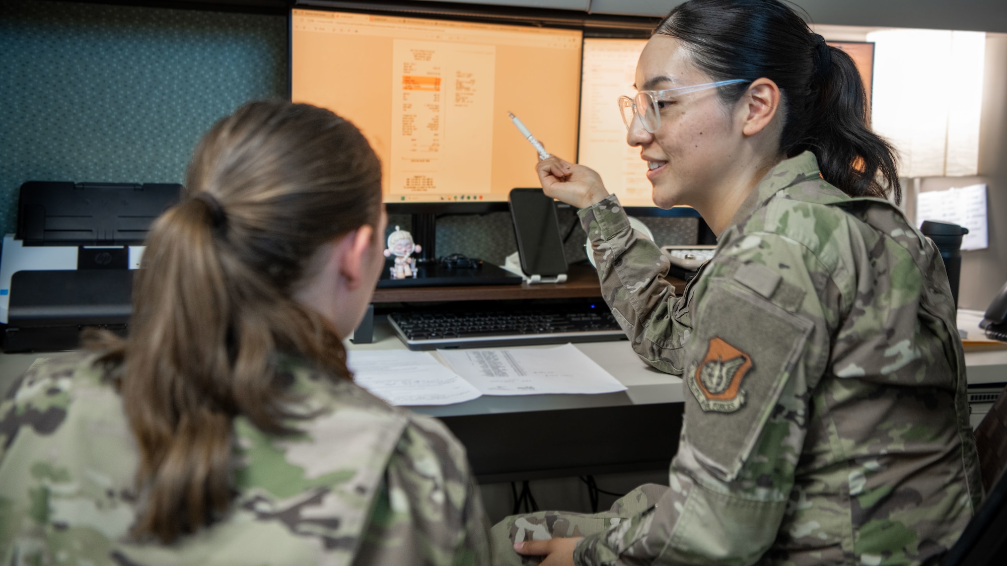 Two women in uniform review content on a computer screen.