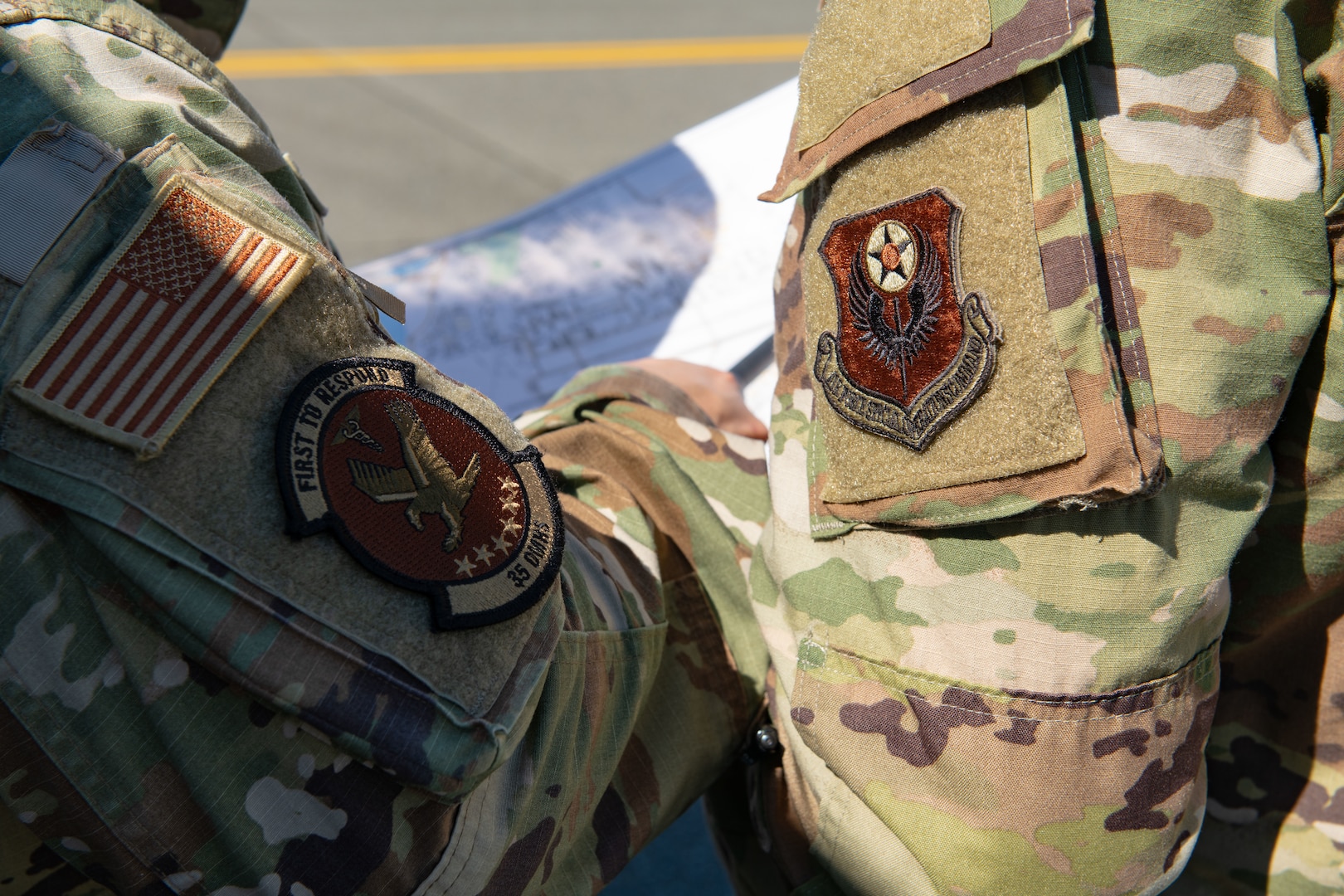 Two uniformed men with decorated patches on their sleeves point at a map.