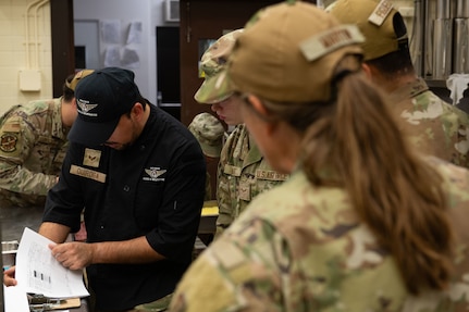 U.S. Air Force Senior Airman Fabrico Quiroga, 35th Force Support Squadron food services technician, reviews  the cooking instructions for a lunch time menu with food services Airmen assigned to the 137th Special Operations Wing, Oklahoma Air National Guard, Misawa Air Base, Japan, Aug. 13, 2025. Food services technicians focused their training to meet proper safety standards and culinary capability in order to meet overall force readiness and support objectives. (U.S. Air National Guard photo by Staff Sgt. Nicholas Swift)