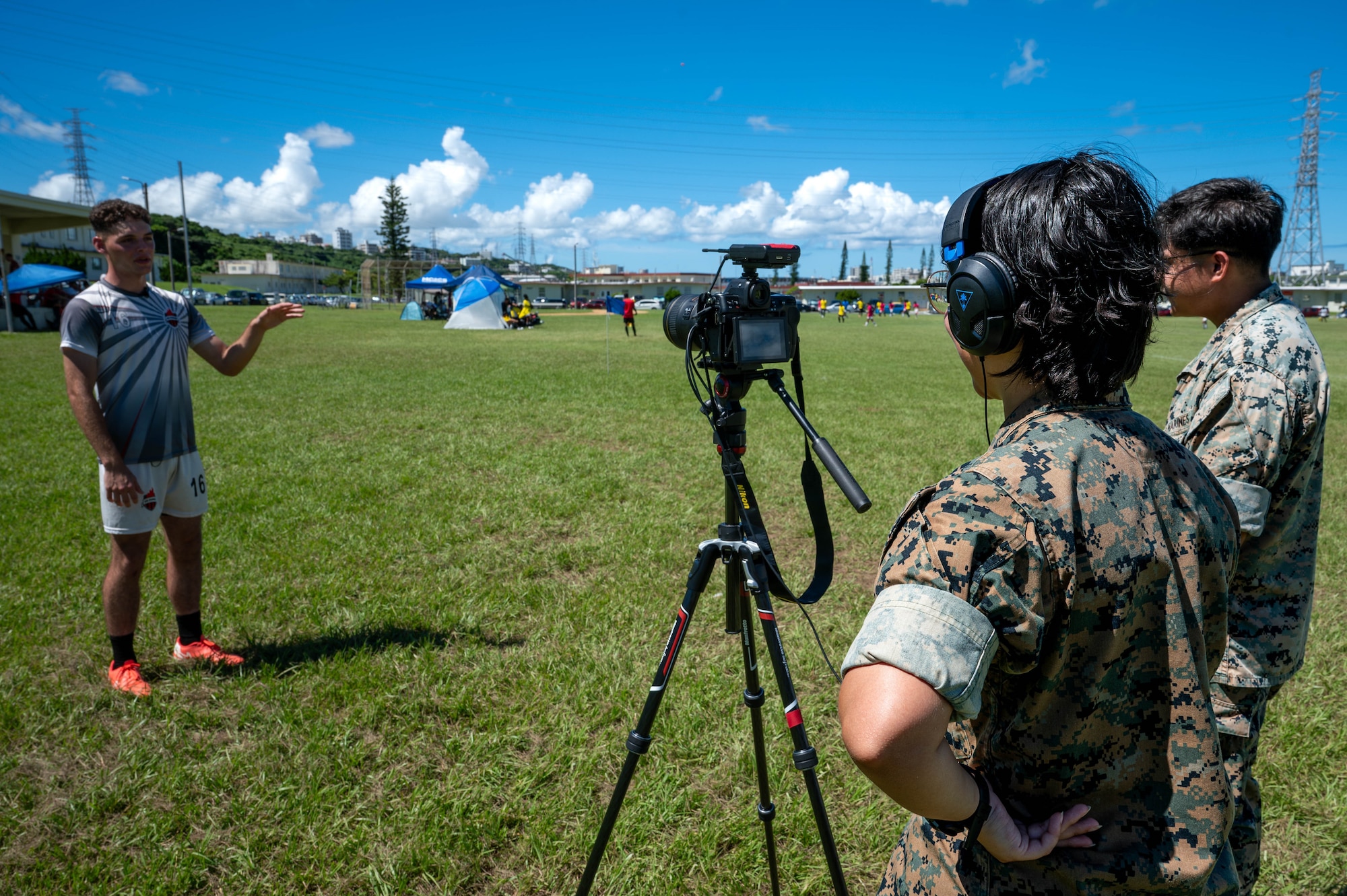 U.S. Marine Corps Sgt. Briana Vera, center, and Cpl. Ernesto Lagunes, American Forces Network Okinawa radio broadcasters, interview a service member during the Marine Corps installation Pacific Joint Service Soccer Match at Camp Foster, Japan, Aug. 27, 2025. AFN attends local events to amplify the voices of service members and strengthen the connection between the base and the community. (U.S. Air Force photo by Airman Nathaniel Jackson)
