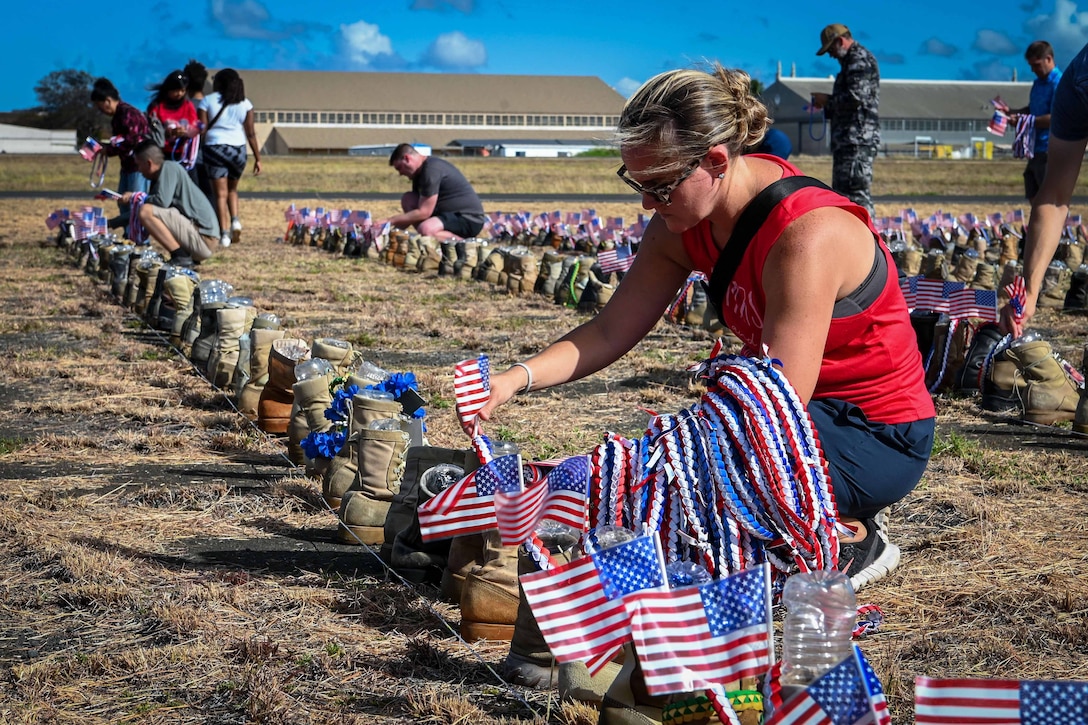 Volunteers place American flags in dozens of boots laid out in a field.