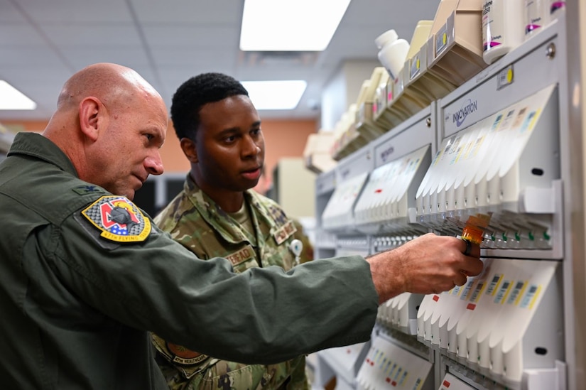 Two uniformed service members stand in military pharmacy and funnel prescriptions into a bottle.