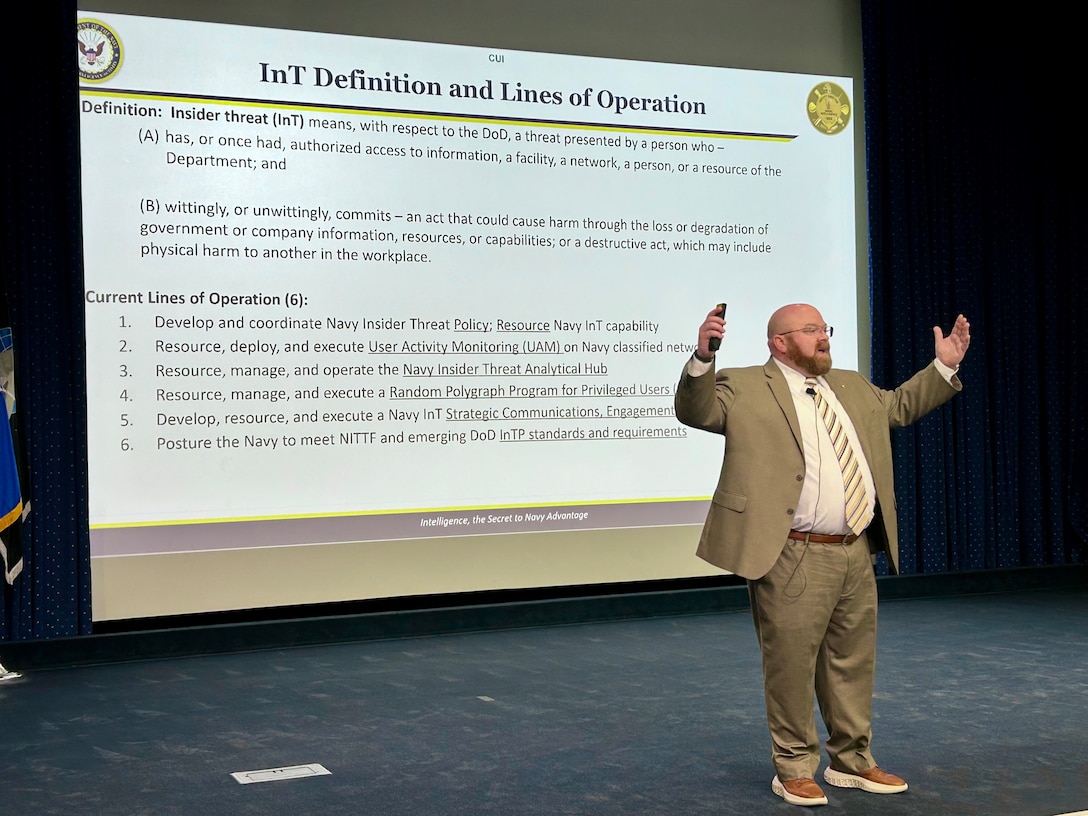 A man stands on a stage in an auditorium speaking to an audience.