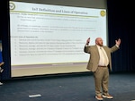 A man stands on a stage in an auditorium speaking to an audience.