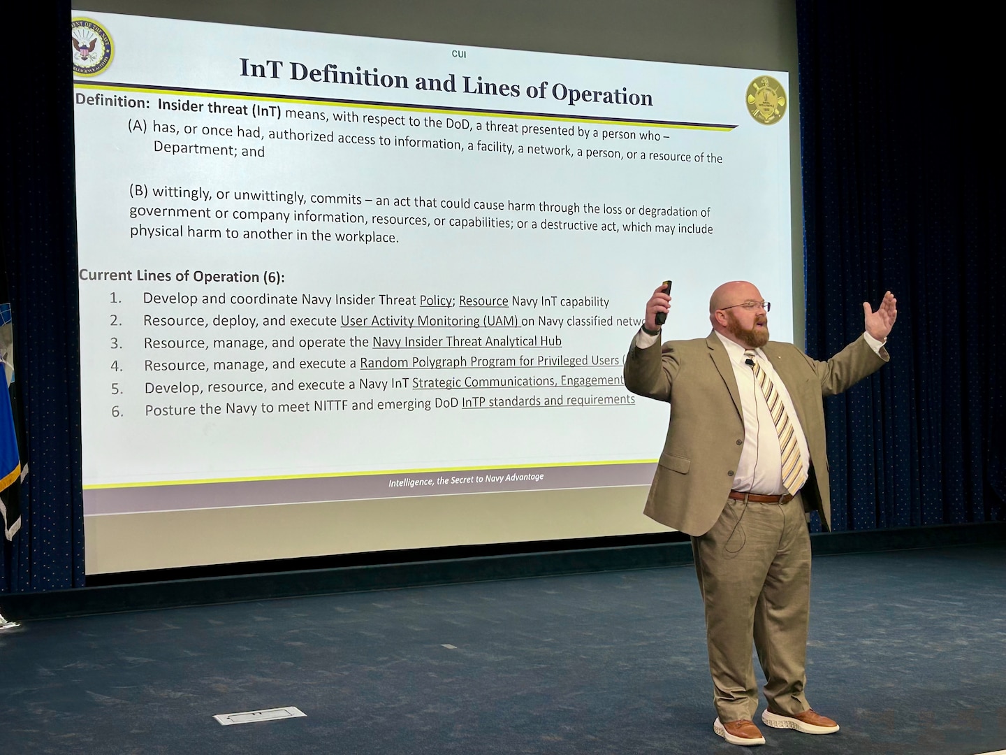 A man stands on a stage in an auditorium speaking to an audience.