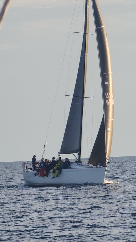Group of sailors sit at the edge of their sailboat as it floats away on the lake.
