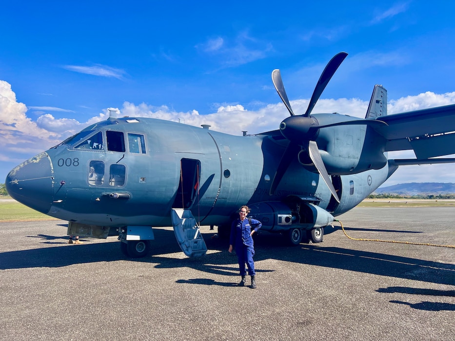Petty Officer 2nd Class Nathalie Aviles stands with a Royal Australian Air Force C-27J Spartan airplane in Honiara, Solomon Islands, following a flight on Aug. 12, 2025.