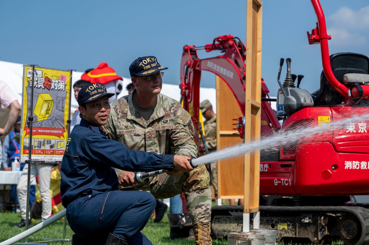 A U.S. Air Force member and a Japanese Fire Department member spray water out of a hose.