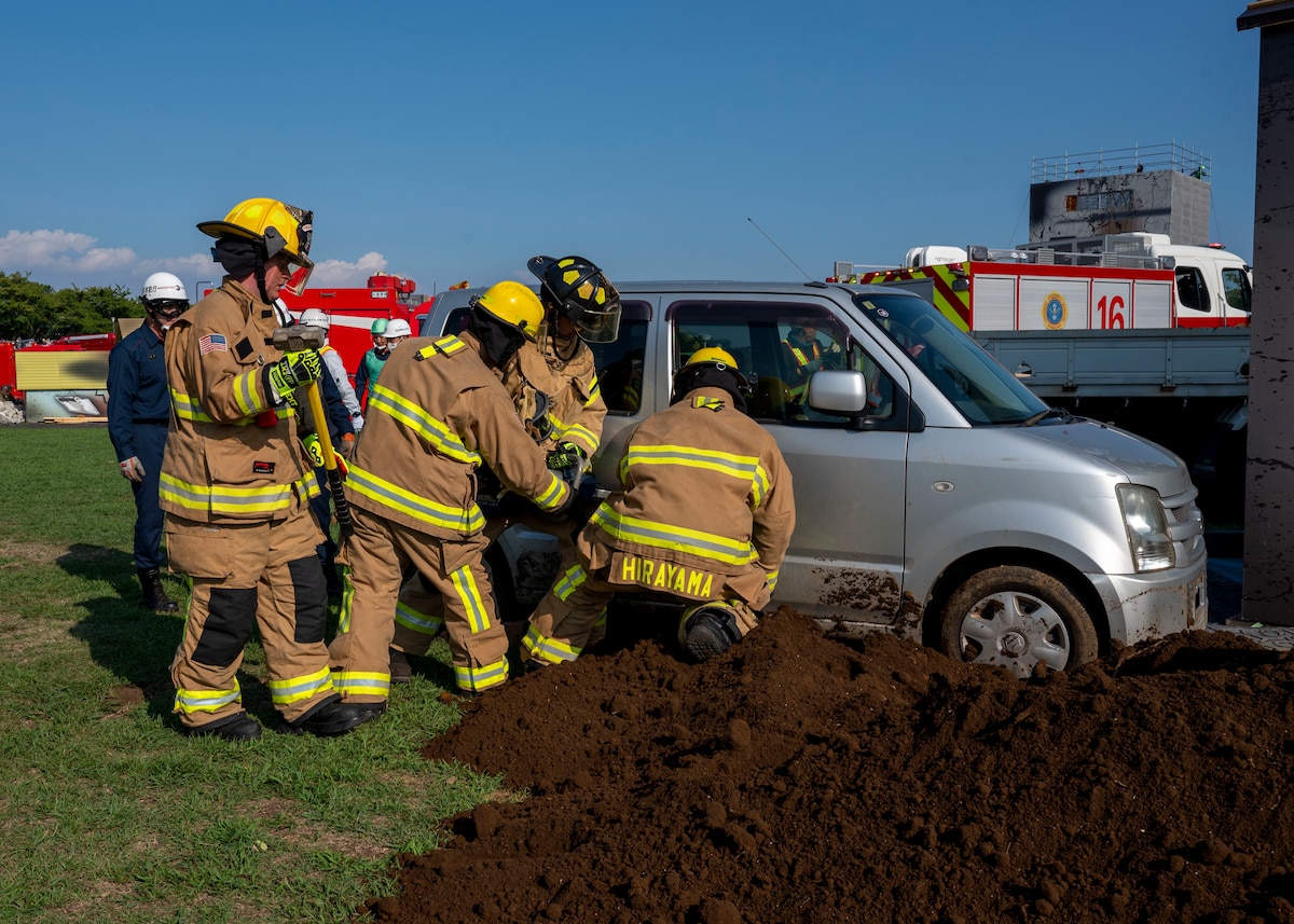 Four U.S. Air Force firefighters conduct an extraction on a silver vehicle.
