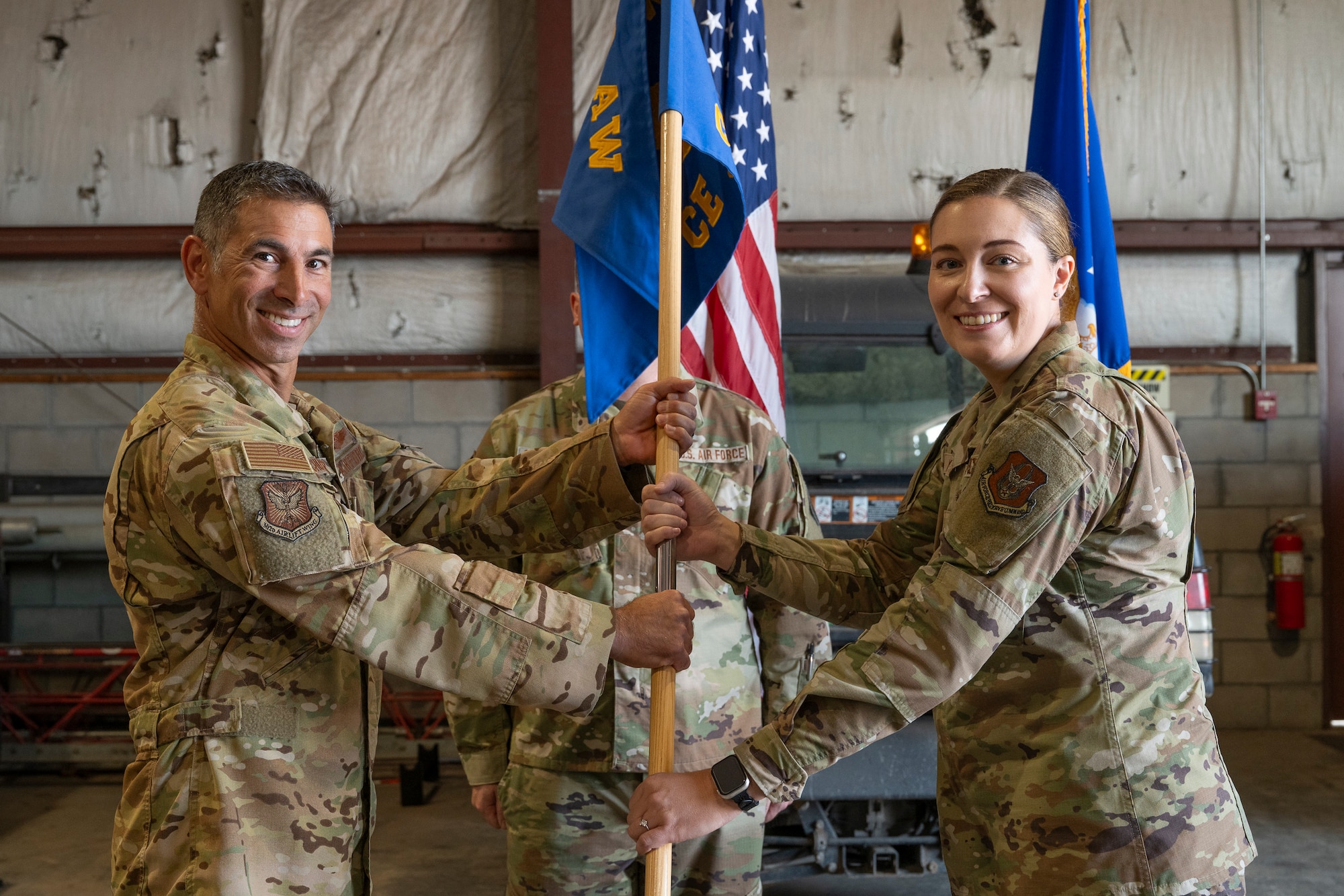Two servicemembers holding a unit guidon flagpole posing for the camera.
