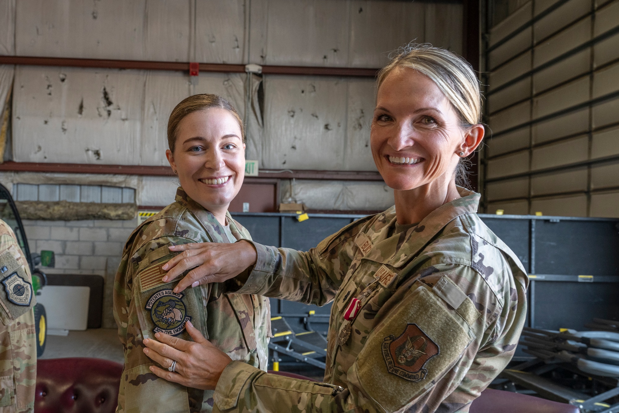 Two military servicemembers, one applying a patch to the uniform of the other.