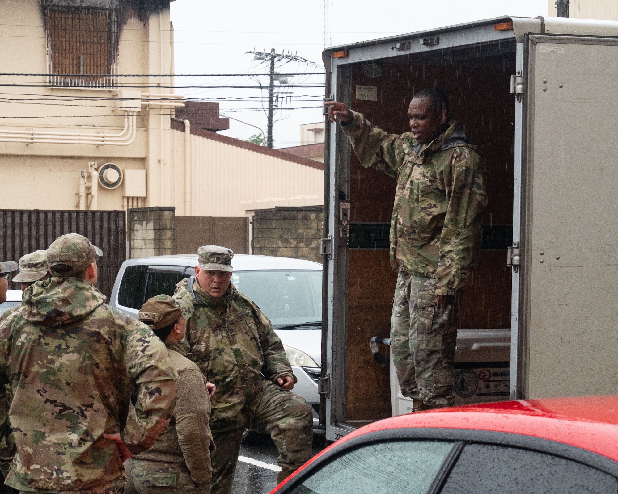 U.S. servicemembers stand inside of and behind a transport vehicle