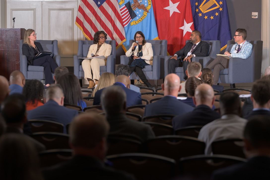 Five panelists sitting in chairs on stage.