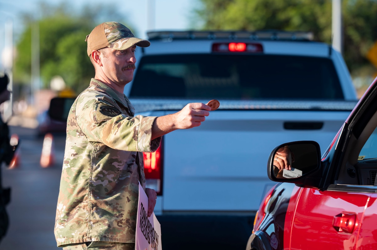 U.S. Air Force Master Sgt. Keith Holland, 25th Operational Weather Squadron first sergeant, hands a 988 Day token to a driver entering Davis-Monthan Air Force Base, Arizona, Sept. 8, 2025. Each token carried messages of hope to strengthen community bonds and highlight available resources. (U.S. Air Force photo by Airman 1st Class Samantha Melecio)